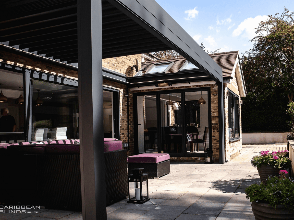 A wall mounted Caribbean Blinds Prestige Pod pergola used as an outdoor dining and living area