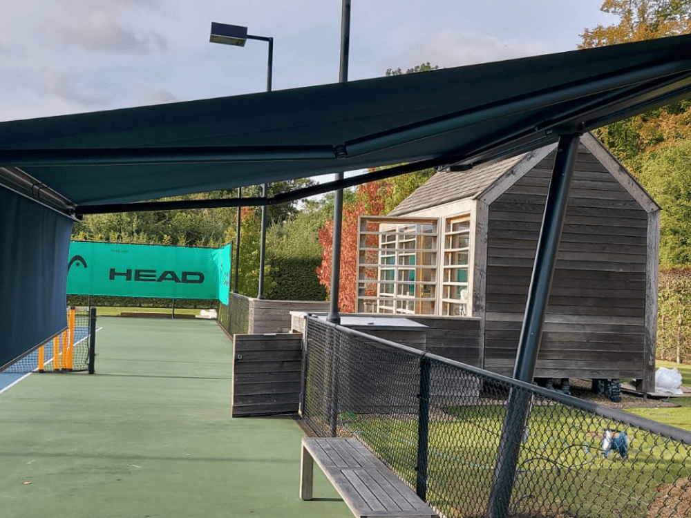 The Markilux Planet freestanding awning with ShadePlus valance and footplates provides functional and elegant sun protection for a tennis court in the Cotswolds, measuring 4.5m wide and 3.5m in projection.
