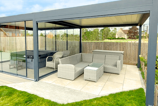 The two freestanding Tarasola Technic's side by side in Grandsborough, Warwickshire, provide a stunning and versatile outdoor space, with one designed to house an outdoor dining and living area, and the other to cover a hot tub, both featuring glass sides fitted with glass sliding doors for an enjoyable and functional outdoor living experience.
