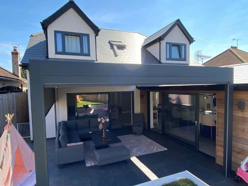 The Tarasola Technic pergola wall mounted to a house in St Albans, Hertfordshire, features added zip screens for shade and privacy, infrared heaters for warmth, and dimmable LED lights for ambiance, providing a comfortable and inviting outdoor space to enjoy year-round.