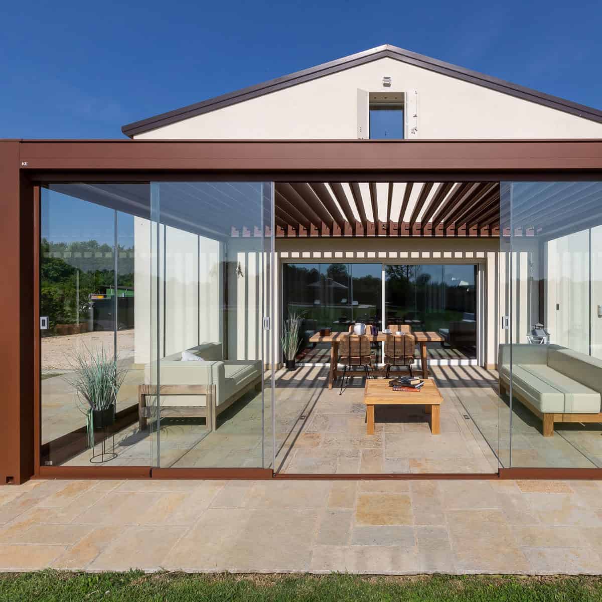Kedry Prime rotating louvred roof in brown on wall-mounted pergola with glass sliding doors