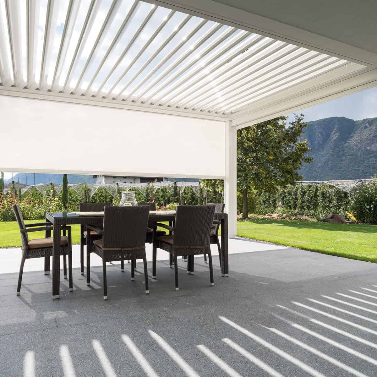 This image showcases the view from inside a KE Kedry Prime louvred roof pergola in white. The adjustable louvres of the Kedry Prime pergola allow for customizable levels of sunlight and shade, creating a comfortable and inviting space to enjoy the outdoors. With its sleek and modern design, the Kedry Prime pergola adds an attractive element to the outdoor space while also providing practical benefits. The white color of the pergola blends seamlessly with the patio and surrounding landscaping, creating a unified and cohesive outdoor living space. The view from inside the pergola highlights the beautiful outdoor environment, with lush greenery and natural light flooding the space. With the KE Kedry Prime louvred roof pergola, you can enjoy the best of both worlds - the beauty of the outdoors with the comfort and convenience of a covered outdoor space.